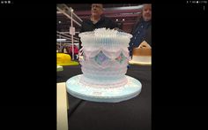 a large white cake sitting on top of a black table next to two men looking at it