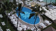 an aerial view of a resort pool with lounge chairs, umbrellas and palm trees