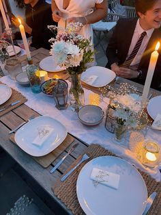 a group of people sitting around a table with white plates and candles on top of it