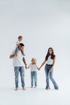 a man and woman holding hands with two small children in front of them, all wearing jeans