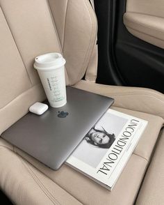 a laptop computer sitting on top of a car seat next to a cup of coffee