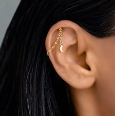 a woman's ear is adorned with gold chains and a crescent shaped nose ring