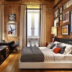 a bedroom with brick walls and wood flooring is pictured in this image, there are pictures on the wall above the bed