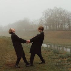 two people holding hands in front of a body of water on a foggy day