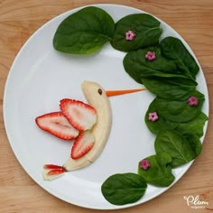 a white plate topped with fruit and veggies shaped like a bird on top of spinach leaves