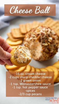 a hand holding a cracker over a plate with cheese ball and crackers on it