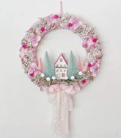 a pink wreath with a house on top and trees in the middle, hanging from a wall