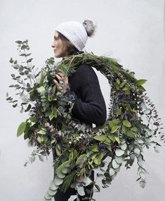 a woman wearing a hat and scarf holding a wreath with greenery around her neck