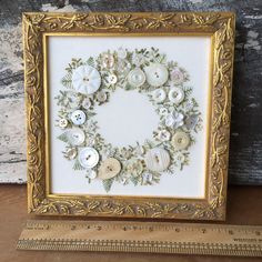 a gold frame with buttons and leaves on the inside is holding a white button wreath