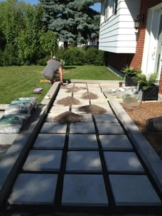 a man is laying bricks on the ground in front of a house with trees and grass