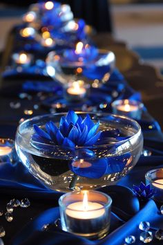 candles are lit in bowls with water and blue ribbon on the table runner, as well as floating lotuses