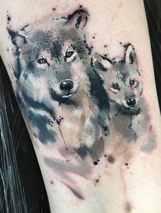 two wolfs tattoo on the arm and leg with watercolor paint splatters