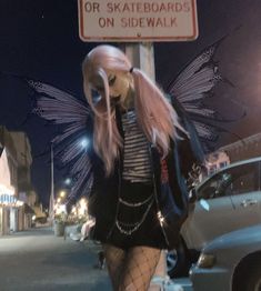 a woman dressed as a fairy standing next to a sign that says no skateboards on side walk