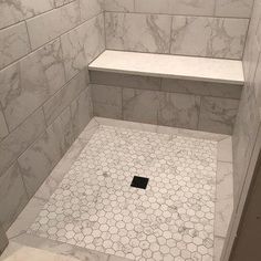 a shower stall with hexagonal tile flooring and white marble tiles on the walls