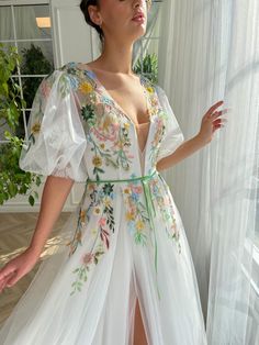 a woman standing in front of a window wearing a white dress with flowers on it