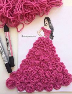 a crochet dress made out of pink yarn and rolled roses next to markers