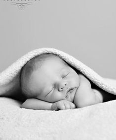 a black and white photo of a sleeping baby wrapped in a blanket with his eyes closed