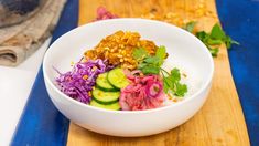 a white bowl filled with food on top of a wooden table next to a cutting board