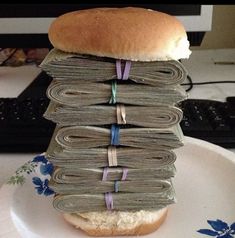 a sandwich sitting on top of a white plate covered in stacks of money next to a computer keyboard