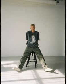 a man sitting on top of a stool in front of a white wall and floor