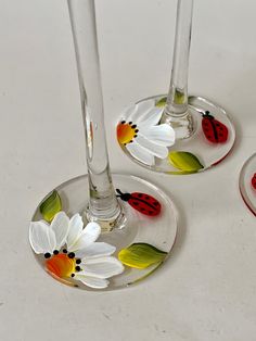 three wine glasses with painted ladybugs and daisies on the bottom one is empty