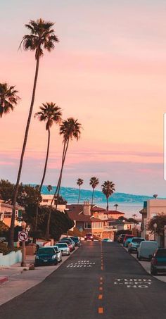 a street with cars parked on both sides and palm trees in the background at sunset