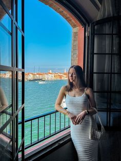 a woman standing in front of a window next to the ocean