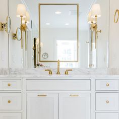 a white bathroom with gold accents and marble counter tops, along with two large mirrors on the wall