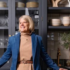 an older woman standing in front of a cabinet with dishes on the shelves behind her