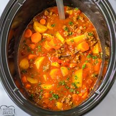 a crock pot filled with stew and carrots on top of a white table