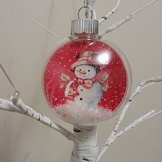 a glass ornament with a snowman on it hanging from a twig