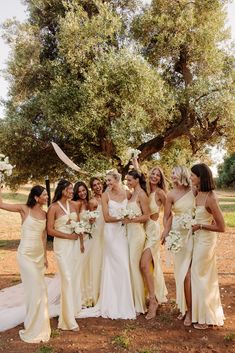 a group of women standing next to each other in front of a tree and holding bouquets