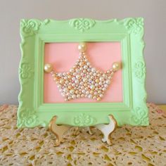 a green frame with pearls and a crown in it on a lace doily table