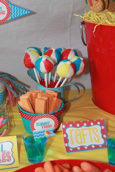 a table topped with lollipops and other candy items next to a red bucket