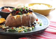 a black plate topped with a baked potato covered in toppings