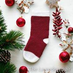 a red and white knitted christmas stocking next to pine cones, fir branches and ornaments