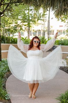 a woman in a white dress and sunglasses posing for the camera with her arms outstretched