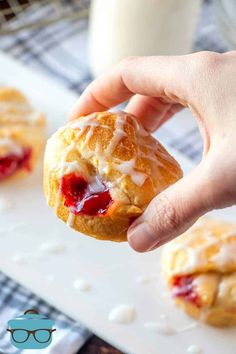 a person holding a pastry with icing and strawberry jam on it in front of other pastries