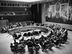 a large meeting room filled with people sitting at round tables in front of a mural