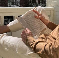 a person sitting in a chair reading a book with their hands on top of the book