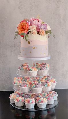 a multi layer cake and cupcakes on a table with flowers in the background