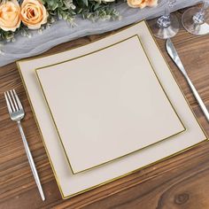 a place setting with flowers and silverware on a wooden tablecloth, next to an empty square plate