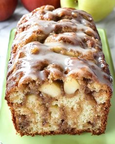 a loaf of cinnamon apple bread with icing on a green plate next to apples