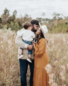 a man and woman holding a baby in their arms while standing in the middle of a field