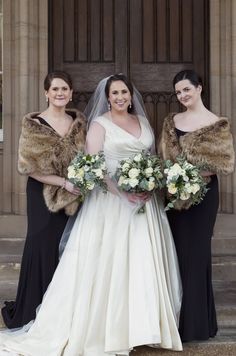 three brides standing in front of a building with fur stolers on their shoulders