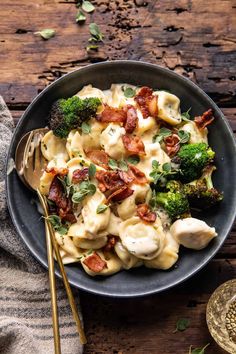 a bowl filled with pasta and broccoli on top of a wooden table next to a fork