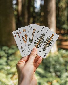 a hand holding four playing cards in front of some trees and bushes on the ground