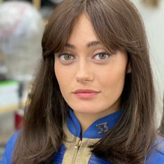 a woman with long brown hair wearing a blue jacket and gold trim around her neck