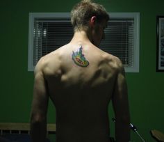 a man with a tattoo on his back standing in front of a green wall and window