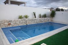 an empty swimming pool next to a white fence and green grass in front of a house